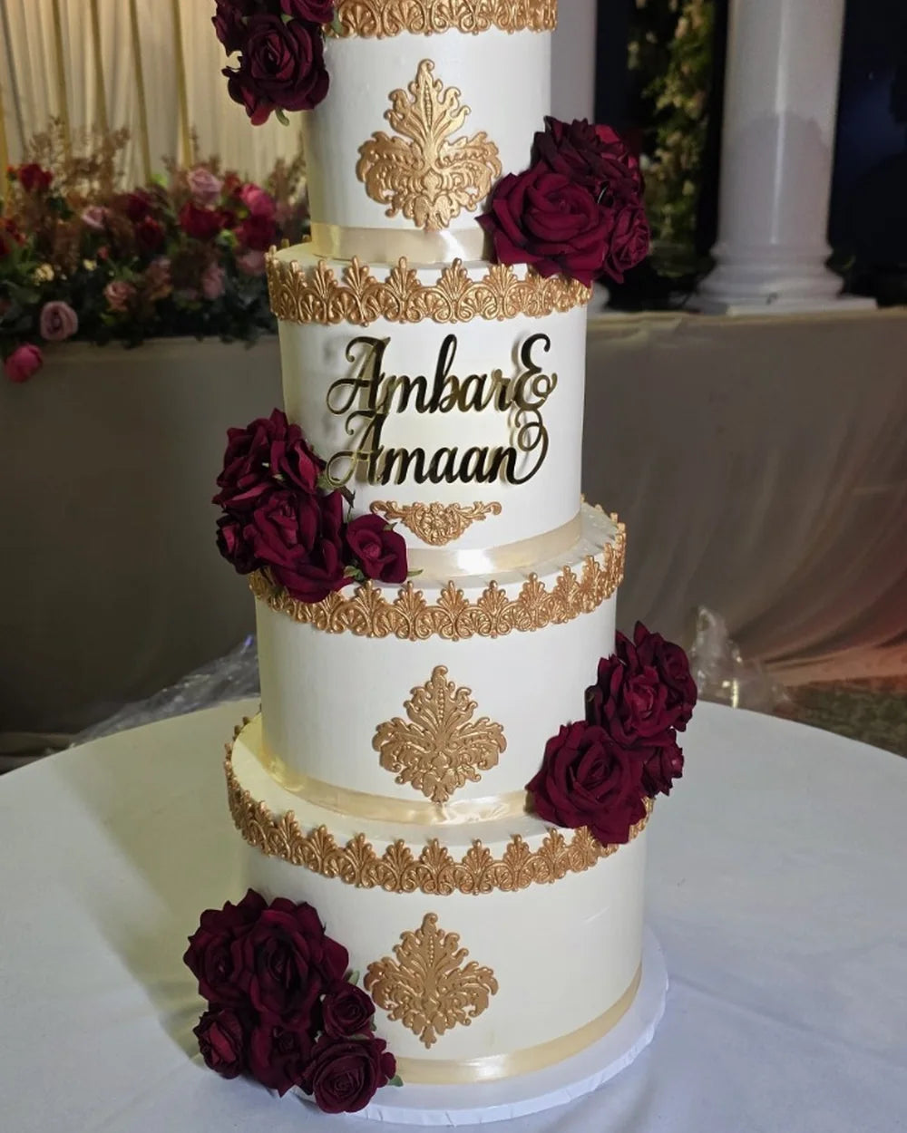Elegant wedding cake with personalised gold names and deep red flowers