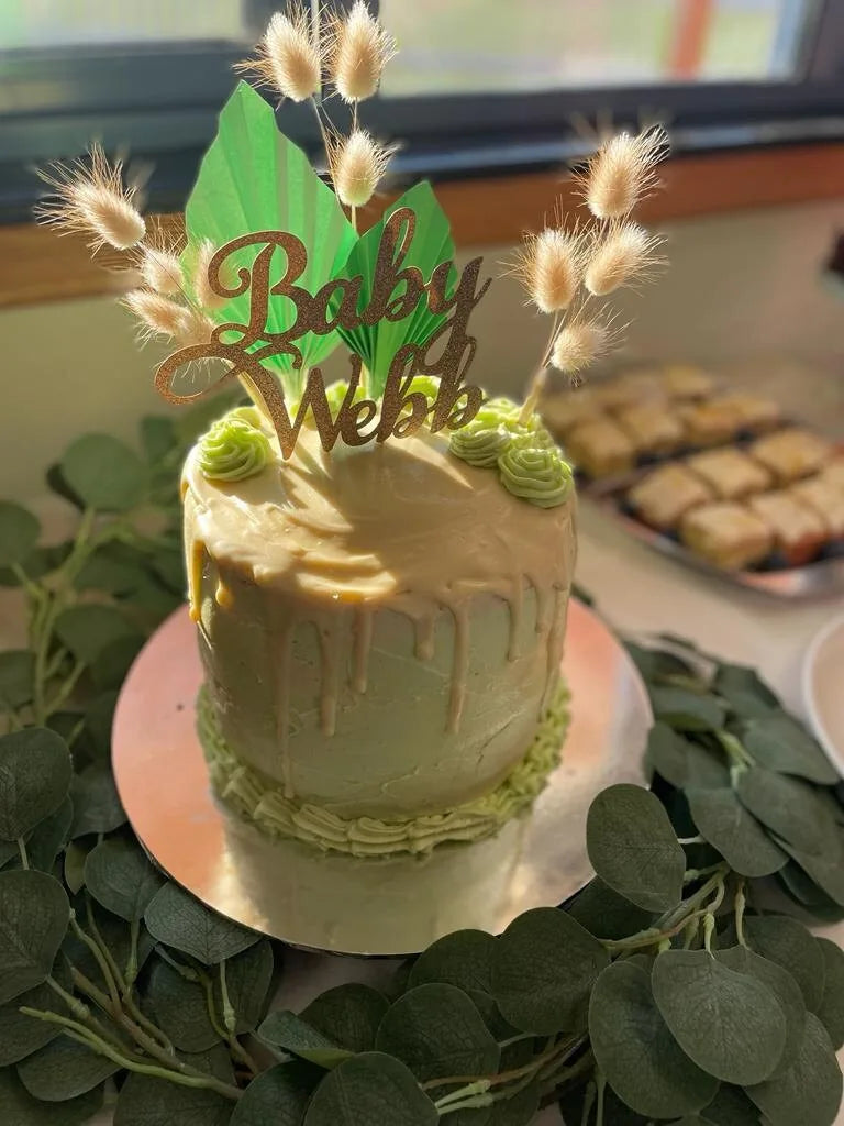 Gold glitter Baby Webb topper on a green and cream baby shower cake